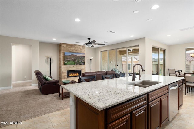 kitchen with light stone countertops, ceiling fan, sink, a center island with sink, and a tile fireplace