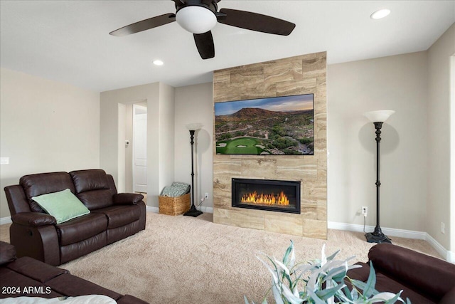 living room featuring ceiling fan, a tile fireplace, and light colored carpet