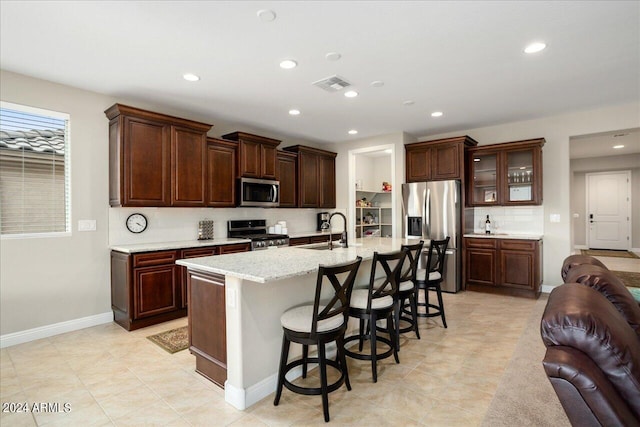 kitchen with a breakfast bar area, stainless steel appliances, a kitchen island with sink, light stone countertops, and sink