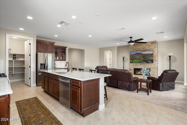 kitchen featuring ceiling fan, a stone fireplace, appliances with stainless steel finishes, sink, and light stone counters