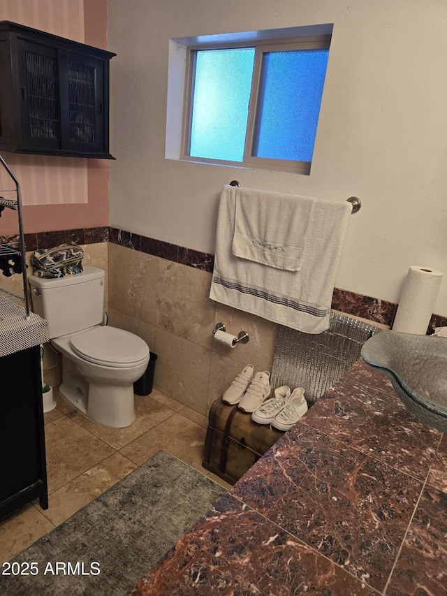 bathroom featuring tile patterned flooring, a wainscoted wall, toilet, and tile walls