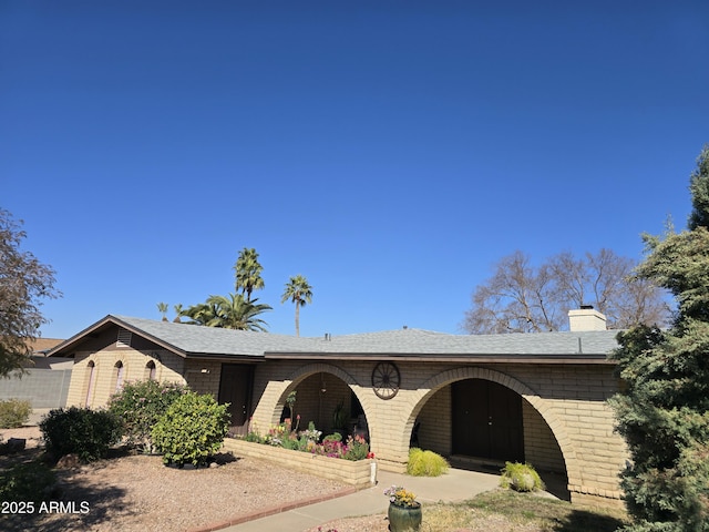 single story home with brick siding, a shingled roof, and a chimney