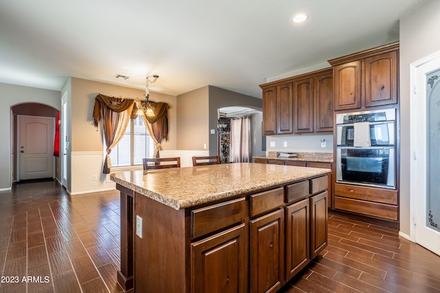 kitchen with dark hardwood / wood-style floors, a chandelier, stainless steel double oven, a kitchen island, and decorative light fixtures