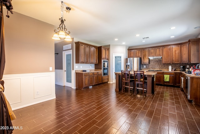 kitchen featuring tasteful backsplash, a breakfast bar, appliances with stainless steel finishes, decorative light fixtures, and a center island