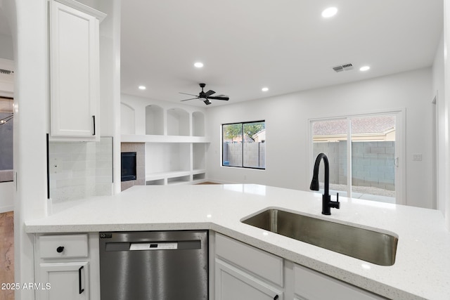 kitchen featuring ceiling fan, a fireplace, stainless steel dishwasher, sink, and white cabinetry