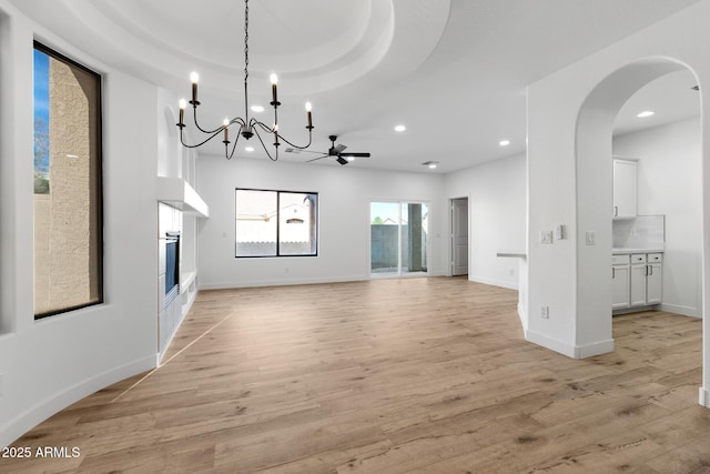 unfurnished living room featuring a raised ceiling, ceiling fan with notable chandelier, and light hardwood / wood-style floors