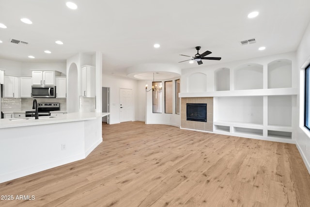 unfurnished living room with ceiling fan with notable chandelier, light hardwood / wood-style flooring, sink, built in features, and a tile fireplace