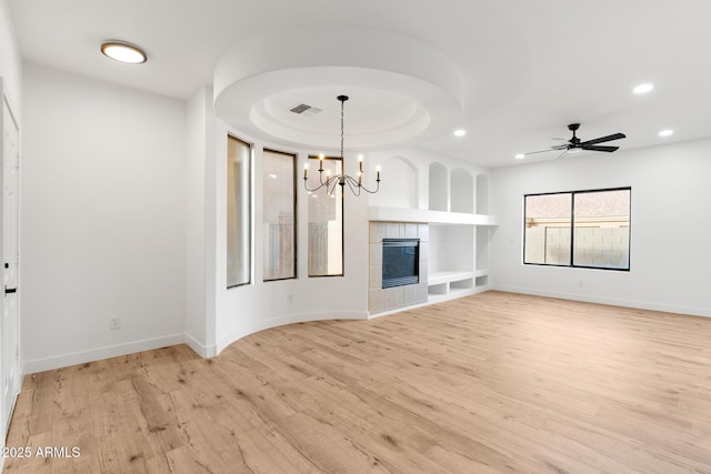 unfurnished living room with ceiling fan with notable chandelier, light hardwood / wood-style floors, and a tiled fireplace