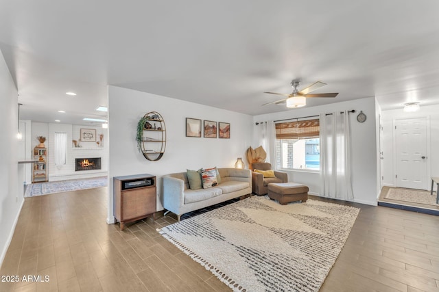 living room featuring a large fireplace, hardwood / wood-style floors, and ceiling fan