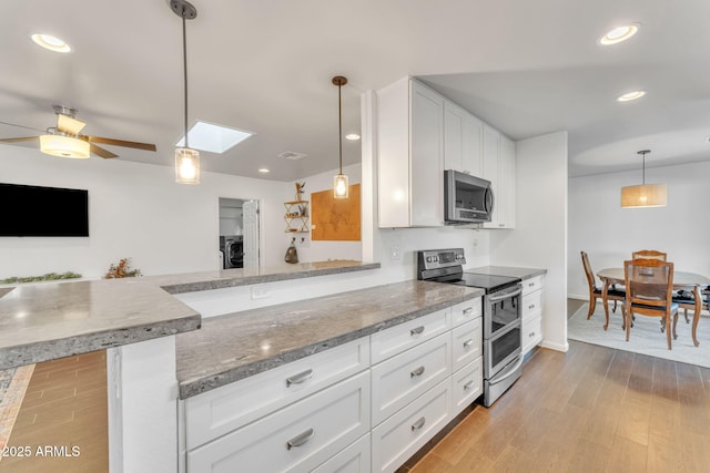 kitchen with decorative light fixtures, kitchen peninsula, white cabinets, and appliances with stainless steel finishes