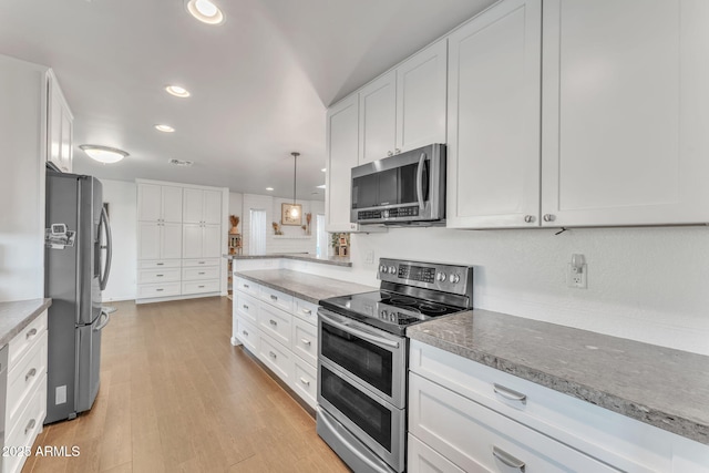 kitchen featuring white cabinetry, stainless steel appliances, decorative light fixtures, and light hardwood / wood-style flooring