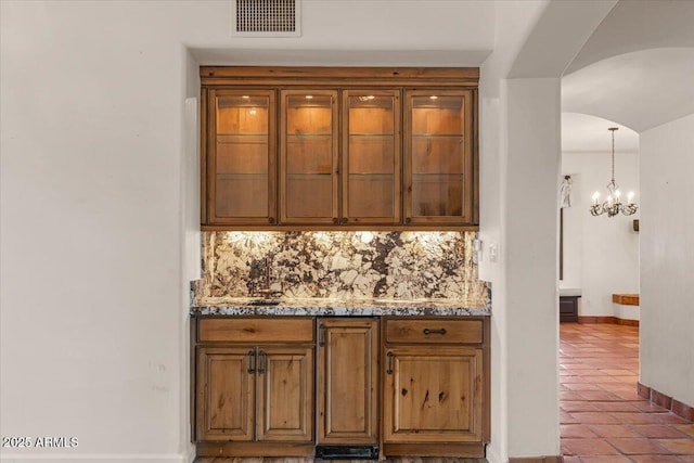 bar featuring decorative backsplash, an inviting chandelier, arched walkways, and visible vents