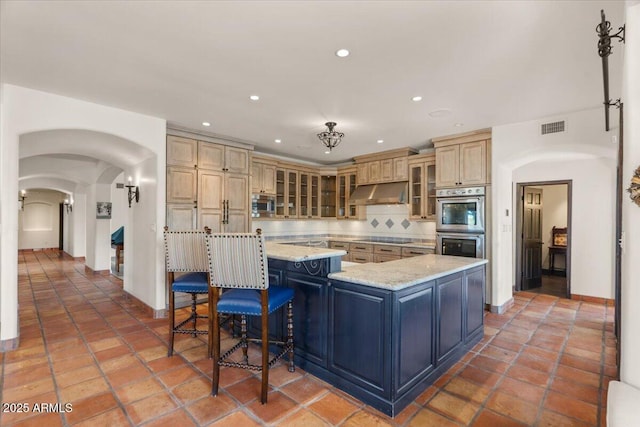 kitchen featuring visible vents, under cabinet range hood, decorative backsplash, appliances with stainless steel finishes, and a large island