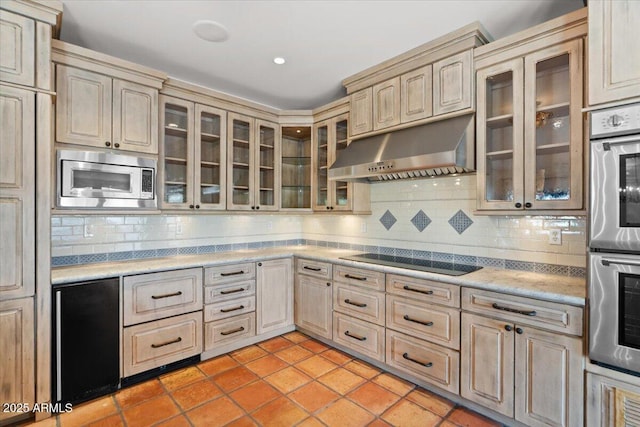 kitchen with under cabinet range hood, stainless steel appliances, glass insert cabinets, and decorative backsplash