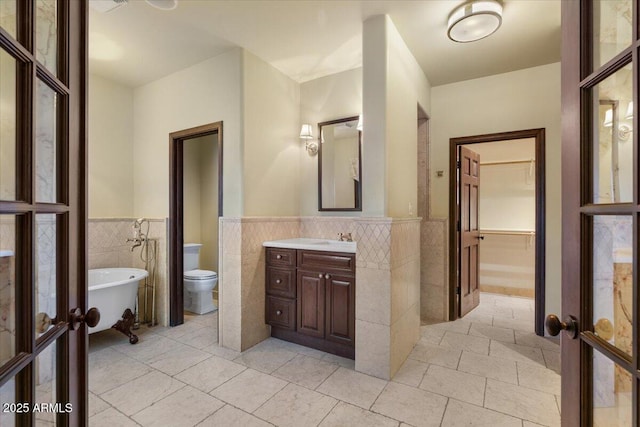 bathroom with a wainscoted wall, french doors, tile walls, and a freestanding tub