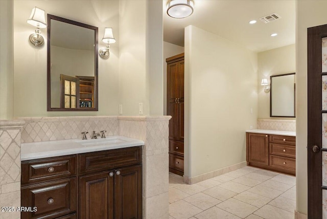 bathroom with visible vents, two vanities, a sink, tile patterned flooring, and tile walls