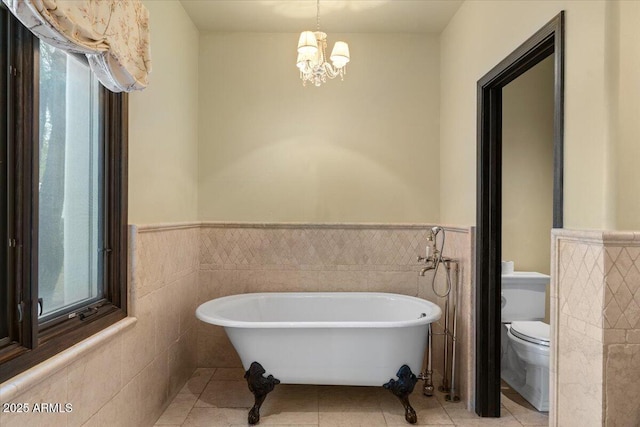 bathroom featuring toilet, an inviting chandelier, wainscoting, tile patterned flooring, and a freestanding bath