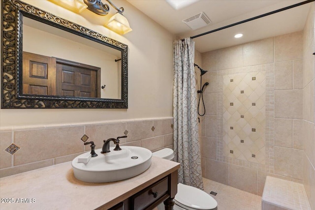 full bathroom with visible vents, a wainscoted wall, toilet, tiled shower, and vanity