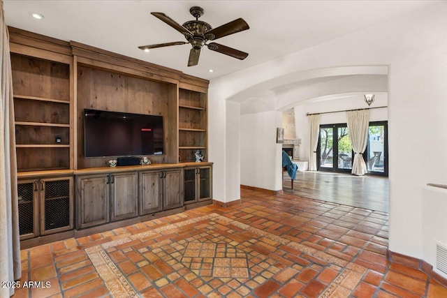 unfurnished living room featuring built in shelves, a fireplace with raised hearth, recessed lighting, baseboards, and ceiling fan