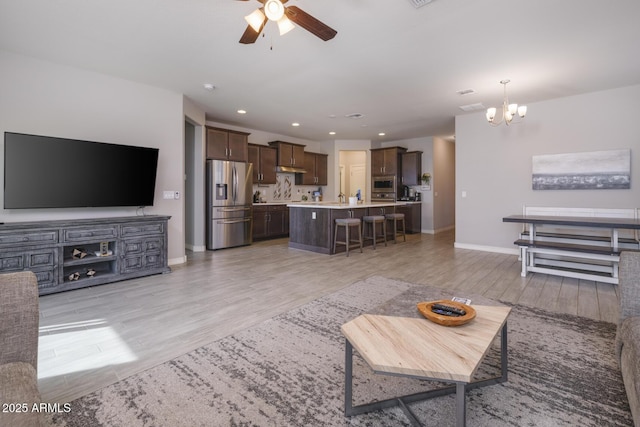 living room with sink, ceiling fan with notable chandelier, and light hardwood / wood-style flooring