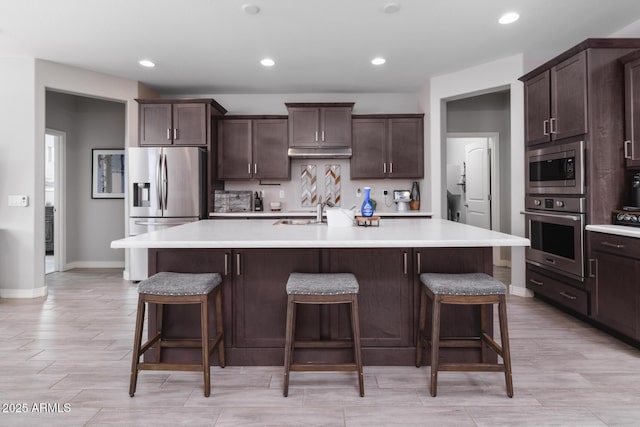 kitchen featuring dark brown cabinetry, stainless steel appliances, a kitchen breakfast bar, and a center island with sink