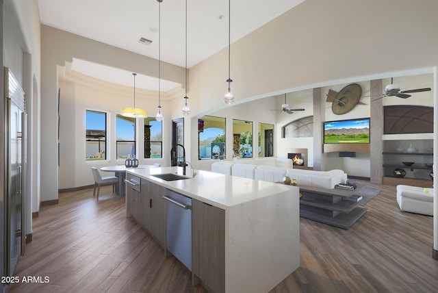 kitchen featuring sink, dark hardwood / wood-style floors, pendant lighting, stainless steel appliances, and a kitchen island with sink