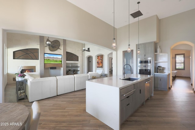 kitchen featuring sink, dark wood-type flooring, ceiling fan, hanging light fixtures, and a center island with sink