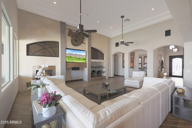 living room with dark hardwood / wood-style floors, a towering ceiling, a fireplace, ornamental molding, and ceiling fan