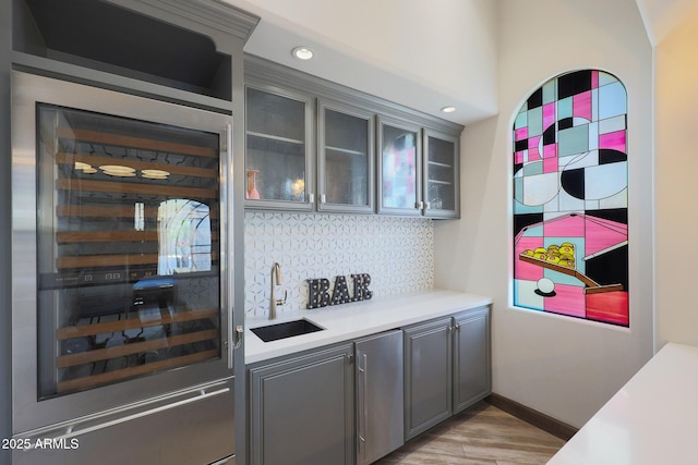 bar featuring beverage cooler, sink, decorative backsplash, and gray cabinetry