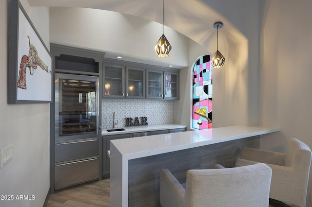 kitchen with pendant lighting, wood-type flooring, kitchen peninsula, and tasteful backsplash