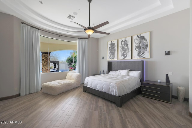 bedroom with a raised ceiling, wood-type flooring, and ceiling fan