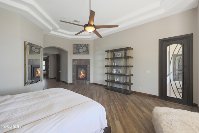 bedroom featuring dark hardwood / wood-style floors, ceiling fan, a tray ceiling, and a tile fireplace