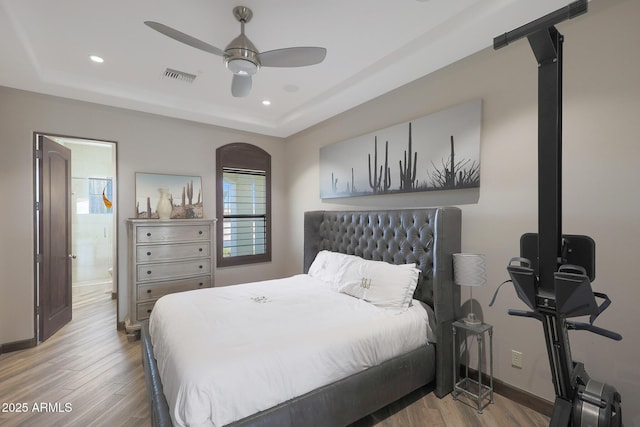 bedroom with a raised ceiling, ceiling fan, light hardwood / wood-style floors, and ensuite bath