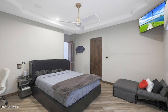 bedroom featuring ceiling fan, a raised ceiling, and light wood-type flooring