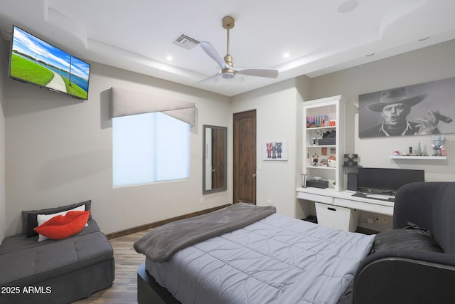 bedroom with hardwood / wood-style floors, a raised ceiling, and built in desk