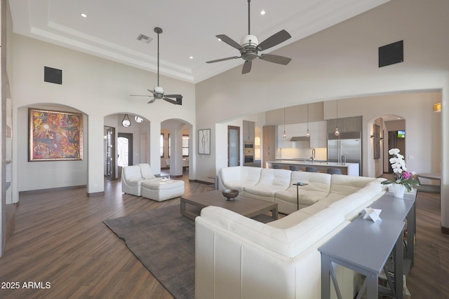 living room with sink, dark wood-type flooring, ceiling fan, and a towering ceiling