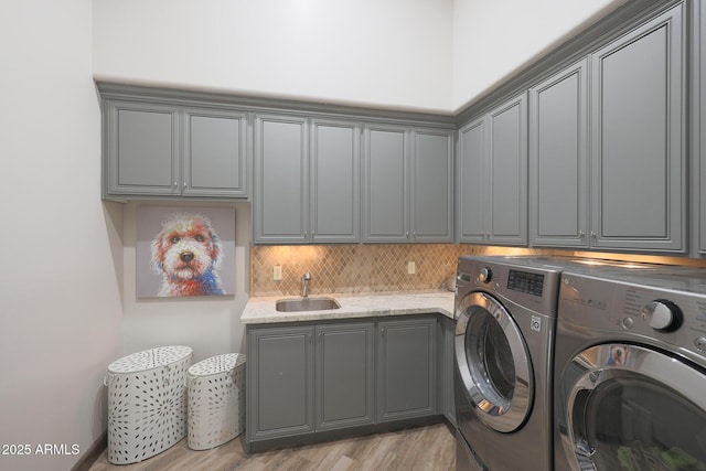 clothes washing area with cabinets, sink, washing machine and dryer, and light wood-type flooring