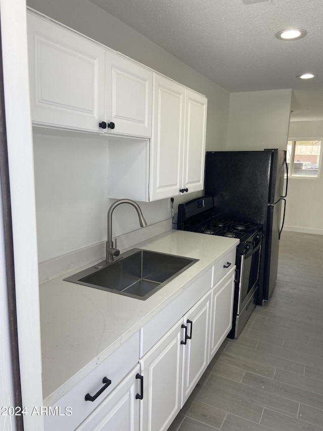 kitchen featuring light stone counters, white cabinetry, a sink, and stainless steel gas range oven