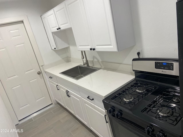 kitchen with stainless steel gas range, sink, white cabinets, and light hardwood / wood-style floors