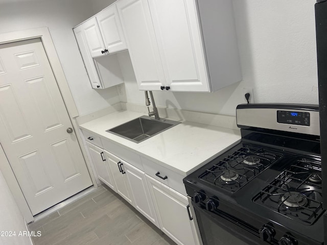 kitchen with black gas range, white cabinetry, light countertops, and a sink