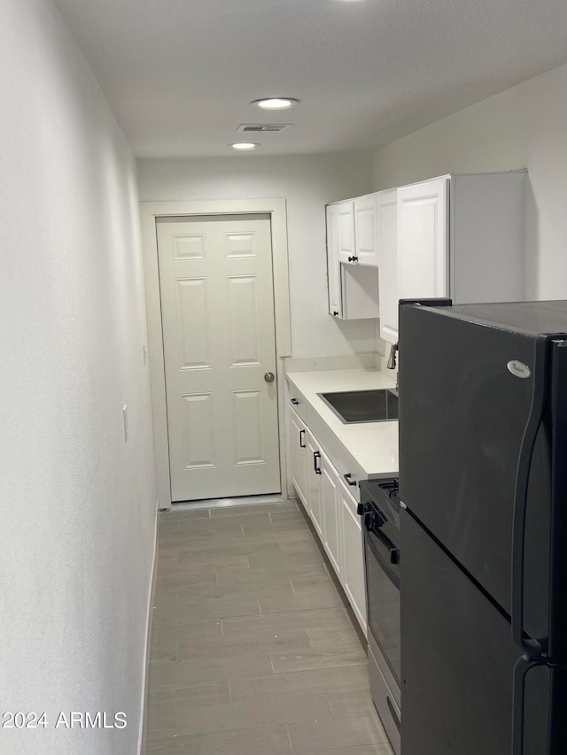 kitchen with white cabinetry, stainless steel range oven, black fridge, sink, and light hardwood / wood-style floors