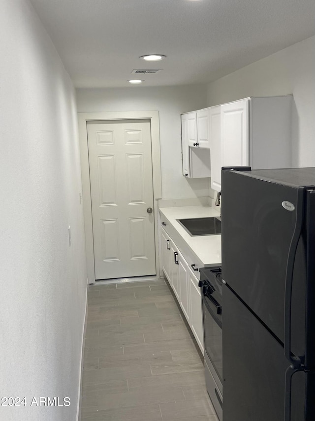 kitchen with stainless steel electric range oven, visible vents, freestanding refrigerator, white cabinets, and a sink