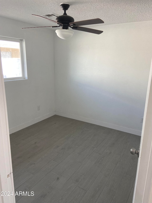 empty room featuring ceiling fan, dark wood-type flooring, and a textured ceiling