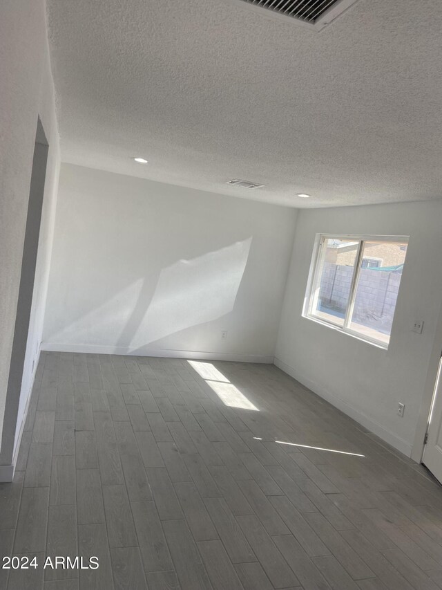 unfurnished room featuring a textured ceiling, visible vents, and wood finished floors