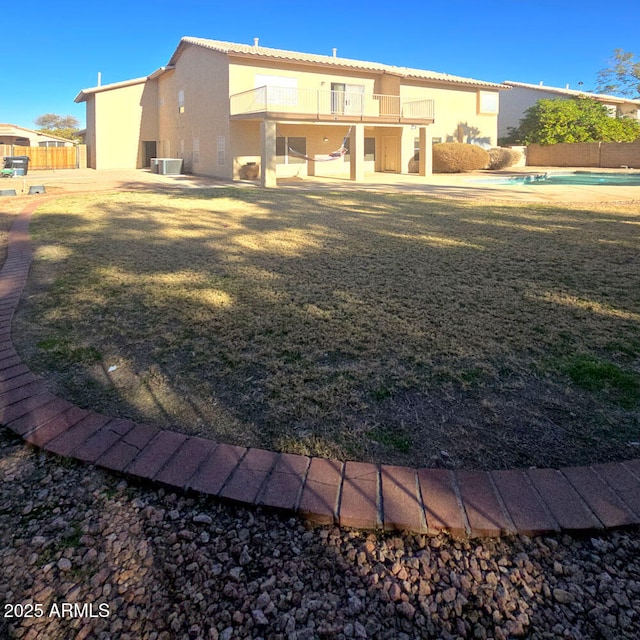 rear view of house featuring a lawn, a balcony, and a patio