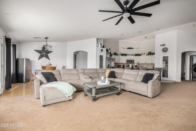 living area with arched walkways, light carpet, a towering ceiling, and a ceiling fan