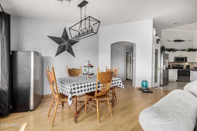 dining space featuring visible vents, arched walkways, baseboards, and light wood-style flooring