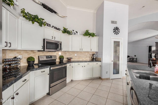 kitchen with light tile patterned flooring, arched walkways, decorative backsplash, appliances with stainless steel finishes, and crown molding