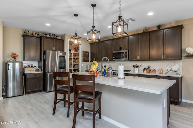 kitchen featuring appliances with stainless steel finishes, dark brown cabinetry, and decorative light fixtures