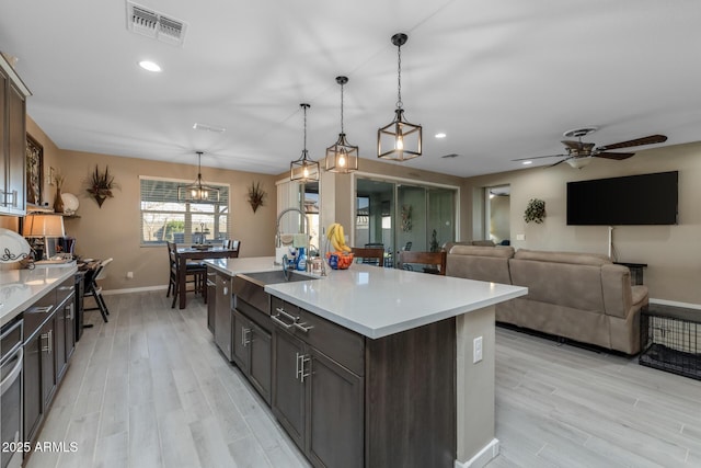 kitchen with pendant lighting, sink, light hardwood / wood-style flooring, dark brown cabinetry, and an island with sink